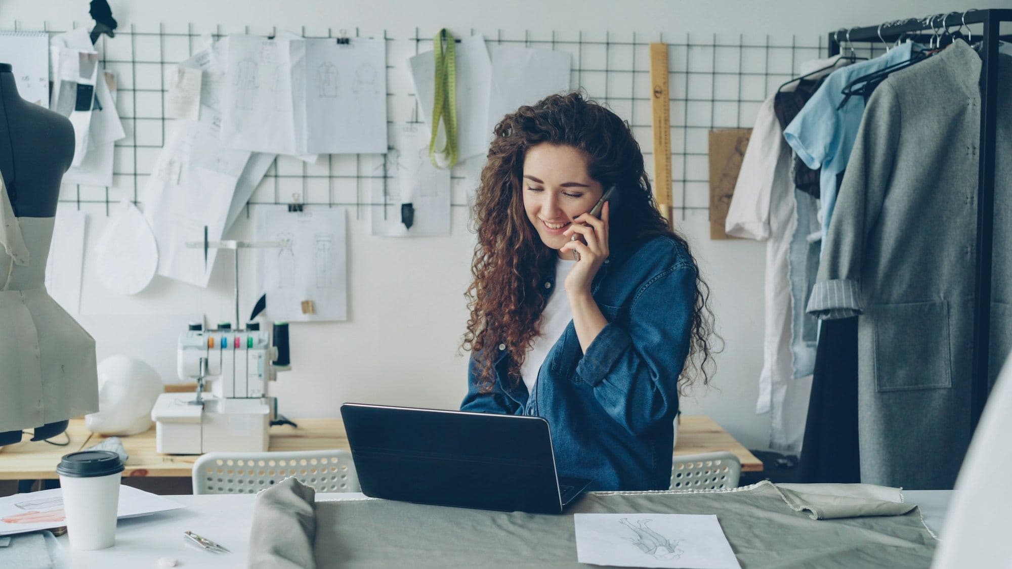 A designer on the phone at her laptop in a clothing studio